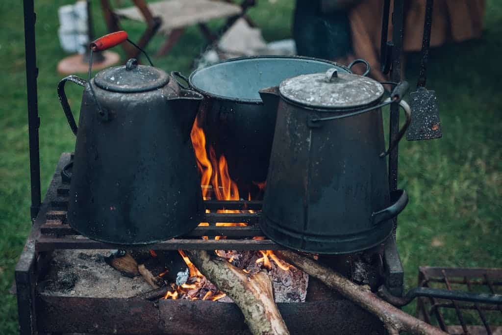 Camp kettles and pot over open fire at an outdoor campsite, ideal for rustic cooking themes.